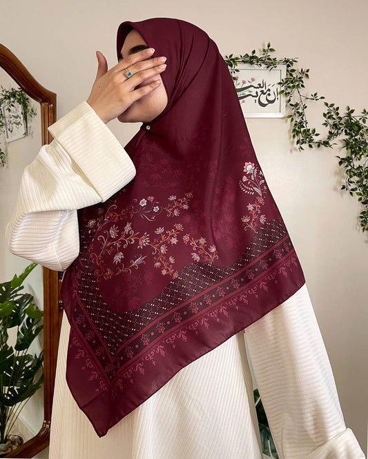Front view of a modern modest woman elegantly wearing the Hadiyah Khamrat Al Ward rich burgundy hijab with complex floral patterns.